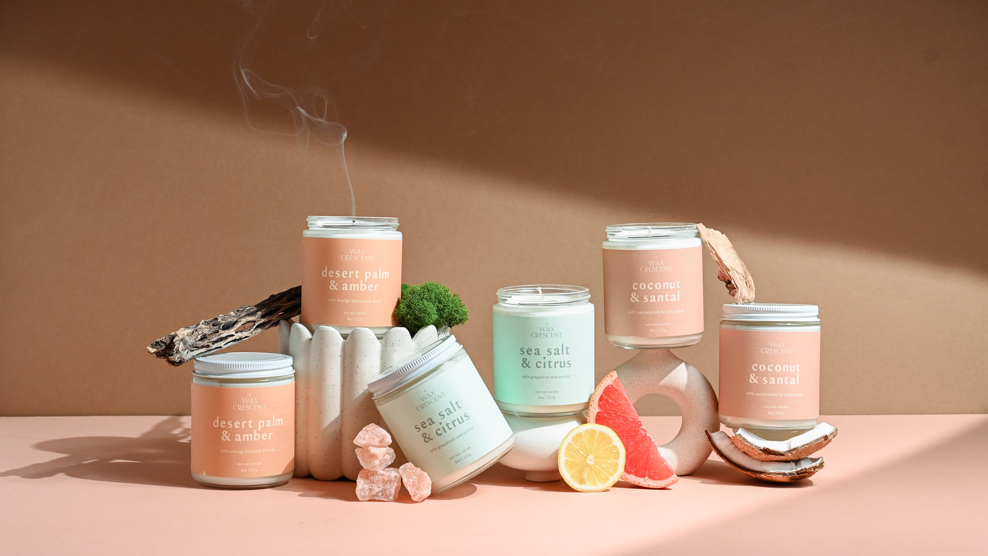 Golden Summer Bundle by Wax Crescent featuring three soy candles—Desert Palm & Amber, Sea Salt & Citrus, and Coconut & Santal—styled with citrus fruit, driftwood, and soft neutral props to evoke a warm, coastal summer vibe.