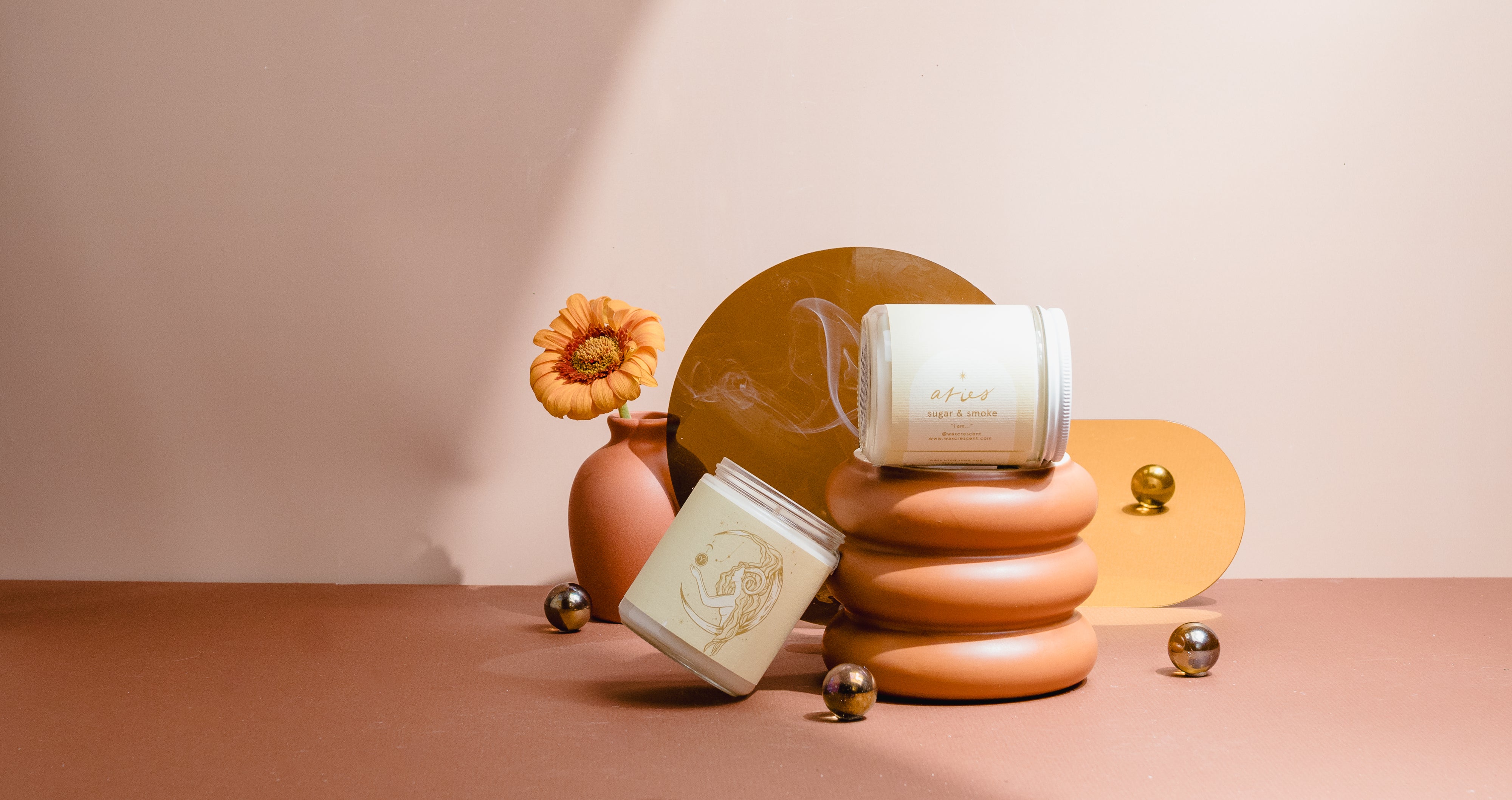 Wax Crescent zodiac candle for Aries with Sugar & Smoke fragrance, styled with gold spheres and sculptural stand