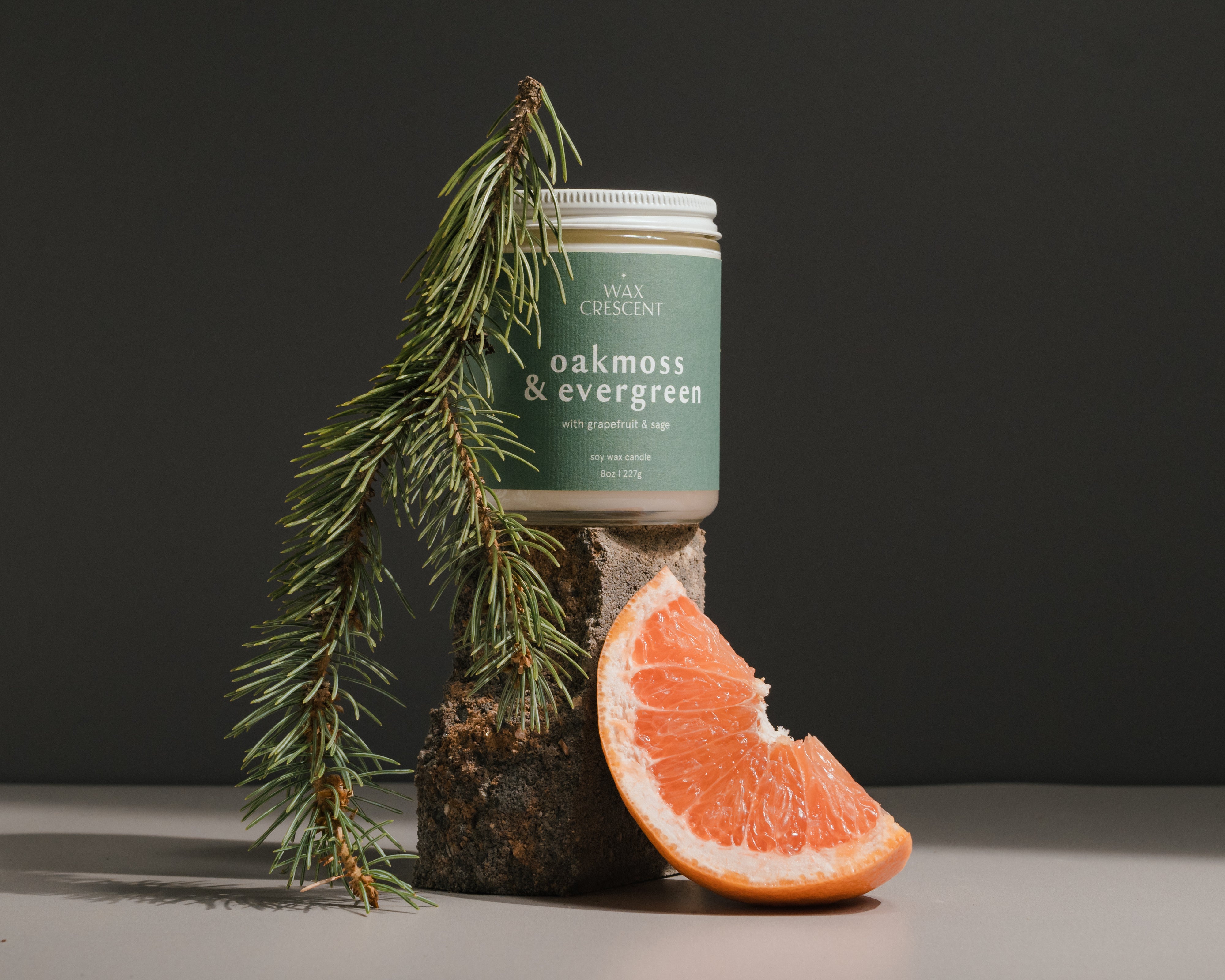 Oakmoss & Evergreen soy wax candle by Wax Crescent, hand-poured in Longmont, Colorado. Candle displayed with fresh evergreen sprigs and a grapefruit slice for a natural, clean-burning aromatherapy experience.