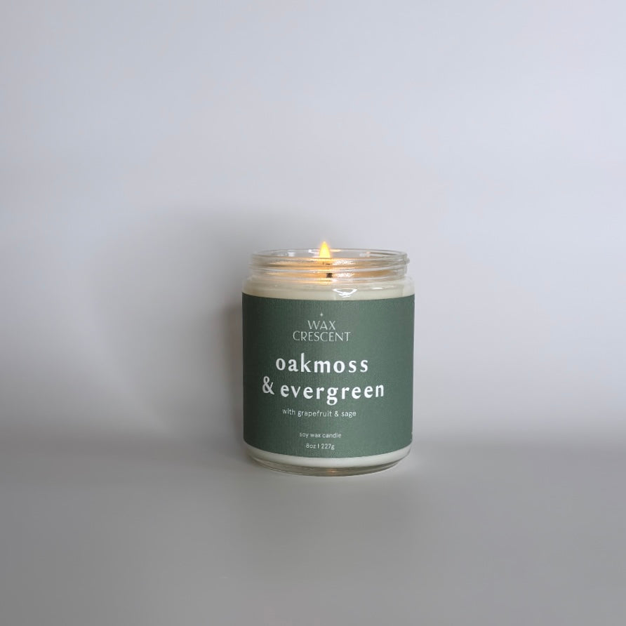 Lit Oakmoss & Evergreen soy wax candle by Wax Crescent on a white background, showcasing its warm glow and inviting aroma. Perfect for creating a cozy atmosphere with natural, clean-burning ingredients.