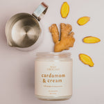 A video showing a small metal steamer cup with milk being frothed, alongside a Cardamom & Cream candle and ginger slices arranged in a circle on a light background.