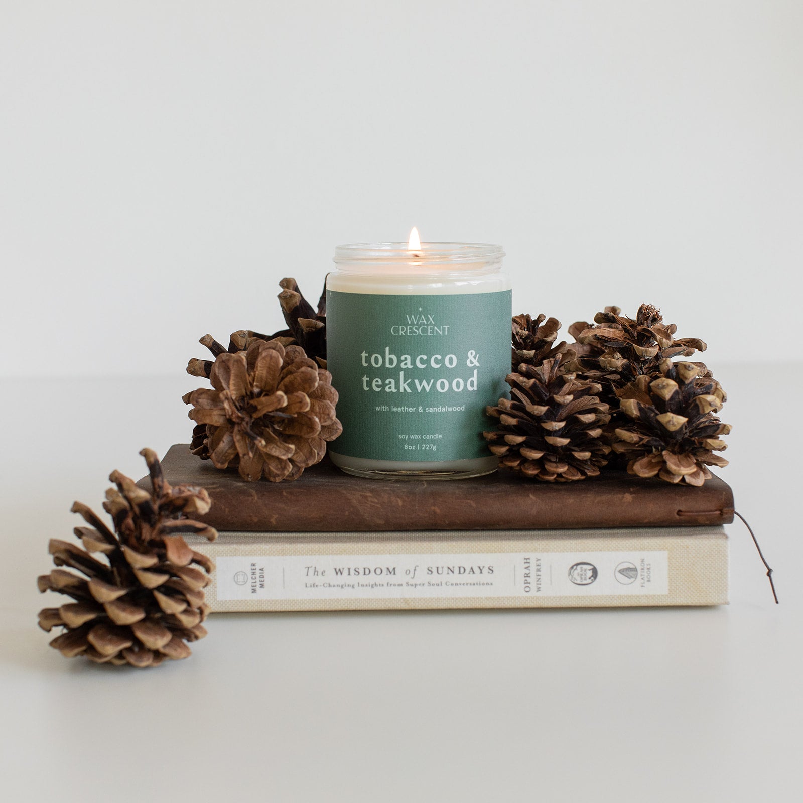 Tobacco & Teakwood candle displayed on a rustic wood slab, surrounded by pine cones, creating a warm and inviting autumn ambiance.