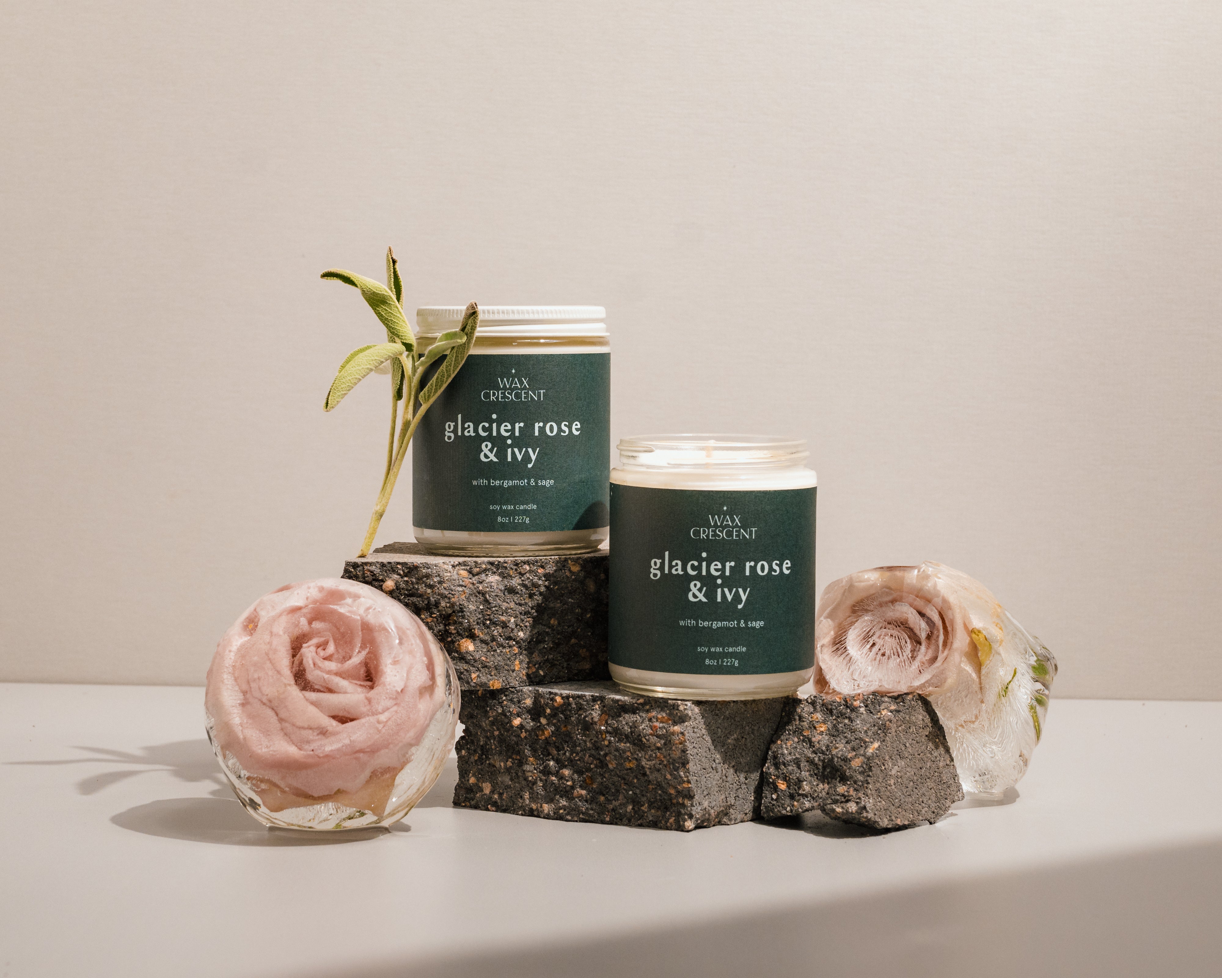 Wax Crescent candles in a minimalist display with floral accents. Featuring the glacier rose & ivy candle in green packaging, perfect for creating a cozy, seasonal ambiance with non-toxic, soy-based scents.