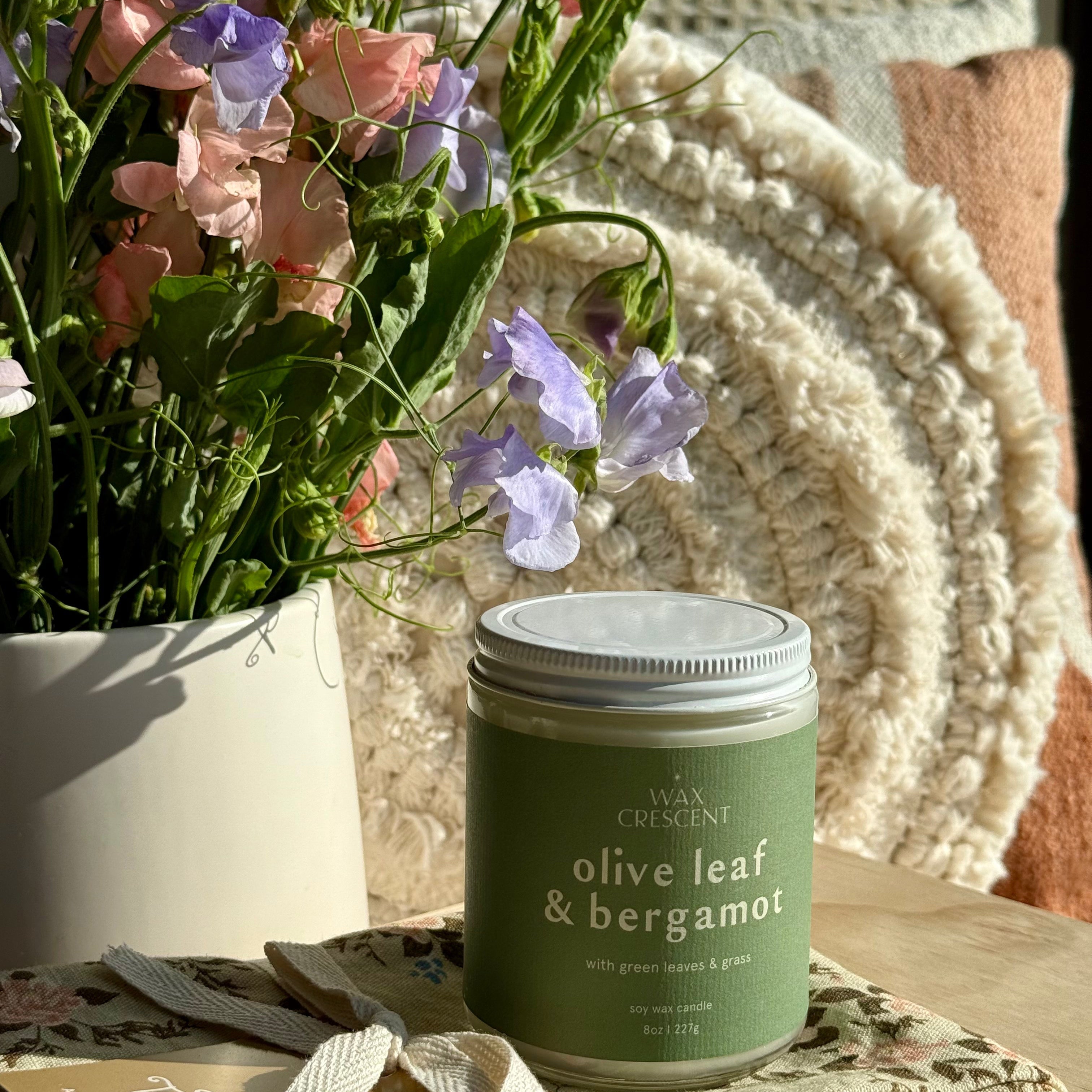 olive leaf & bergamot candle in the evening light surrounded by flowers 