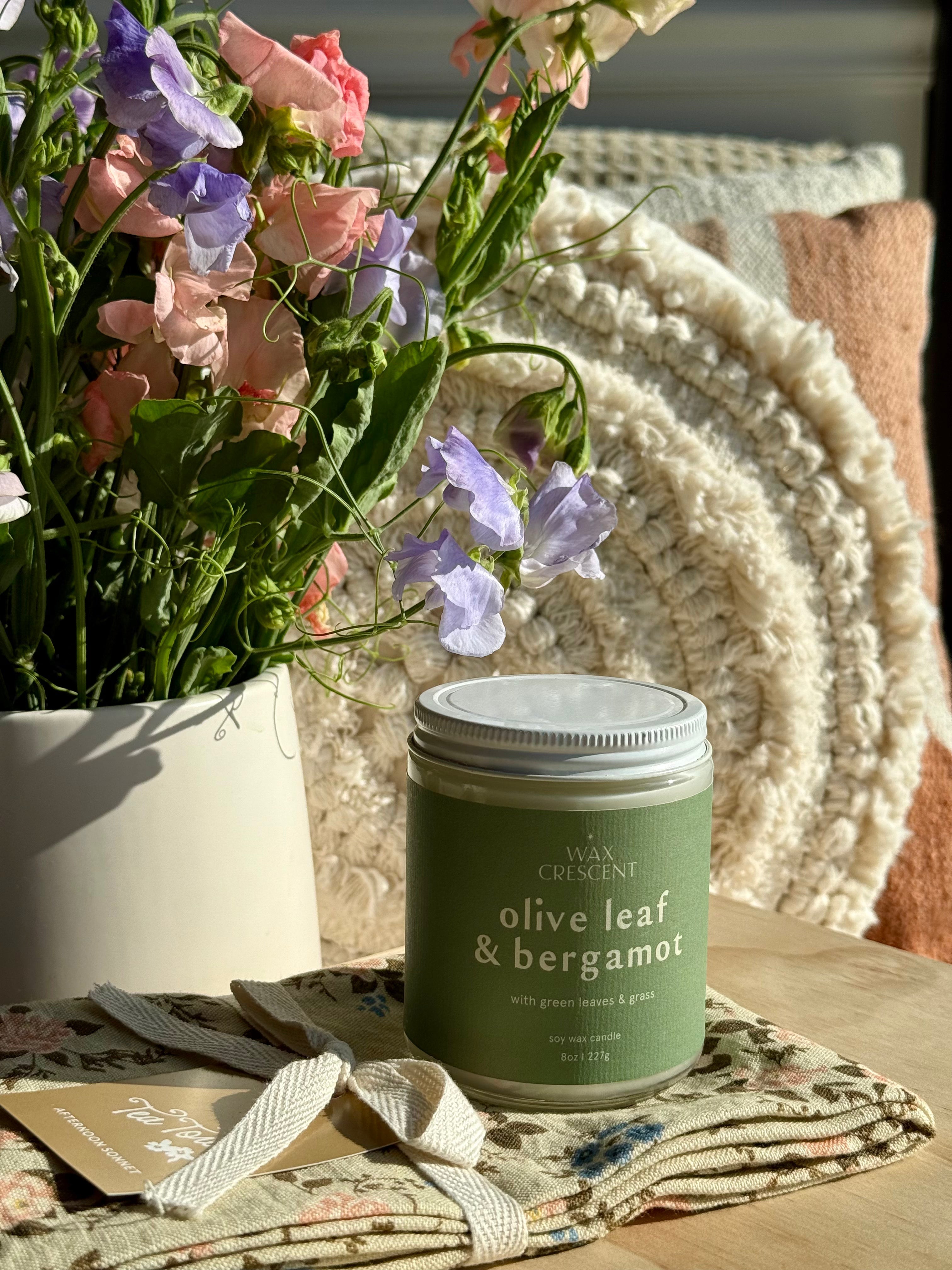 olive leaf & bergamot candle in the evening light surrounded by flowers 