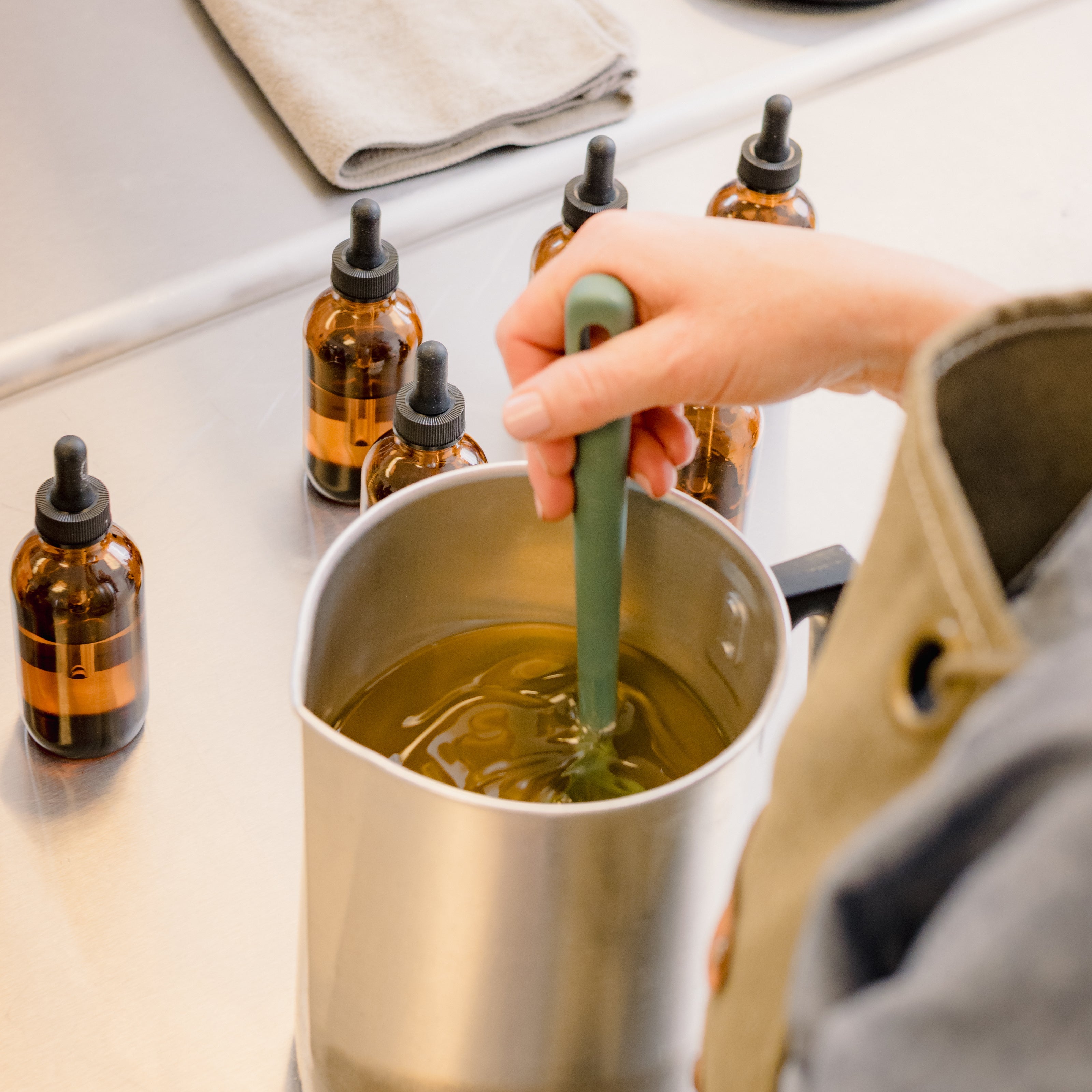 hand crafted soy wax candles image shows a pitcher of wax being stirred and bottles of oil on a stainless steel candle table