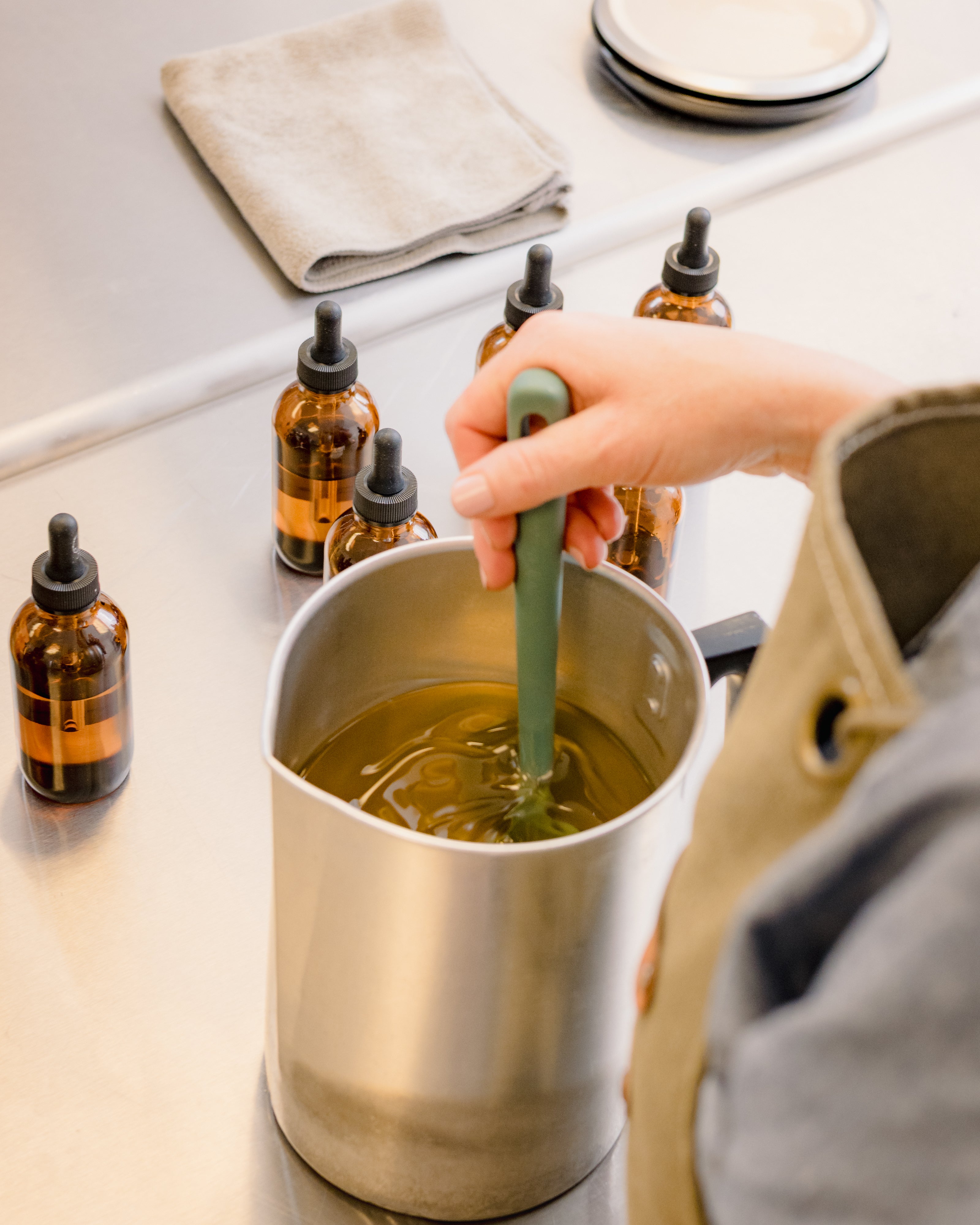 hand crafted soy wax candles image shows a pitcher of wax being stirred and bottles of oil on a stainless steel candle table