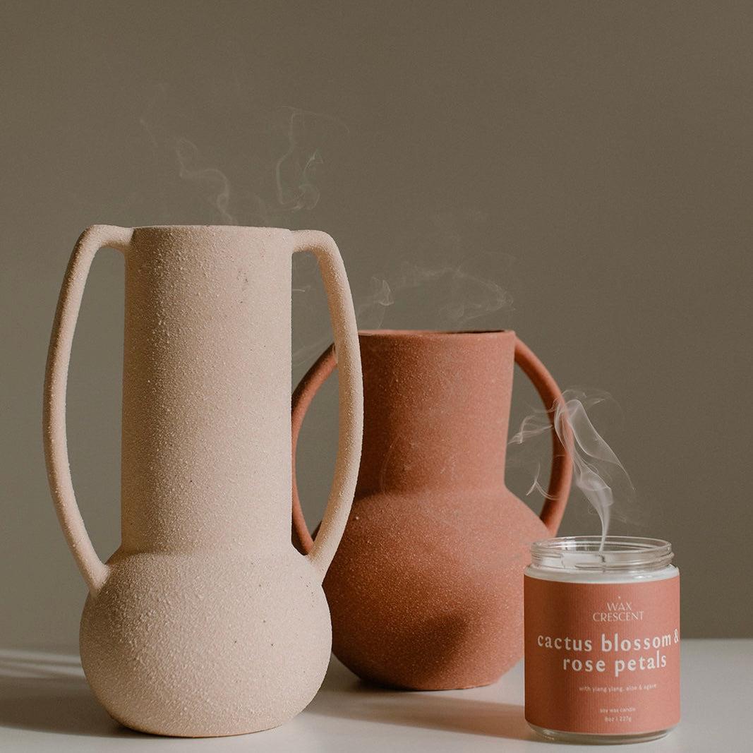 a smoking candle without a flame cactus blossom & rose petals scent next to two light pink vases. 