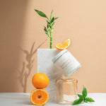 Wax Crescent Bamboo & Bergamot candle styled with fresh oranges, bamboo stems, and natural greenery against a minimalist beige backdrop. A refreshing, spa-like ambiance