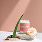 Wax Crescent Cactus Blossom & Rose Petals candle styled with aloe vera, soft pink rose, sand, and natural stones, set against a warm peach-toned background.