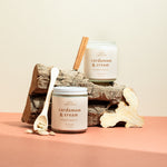 Two Cardamom & Cream soy candles on a wooden log surrounded by cinnamon sticks and cardamom pods — a warm, spiced fragrance hand-poured by Wax Crescent for cozy winter nights.