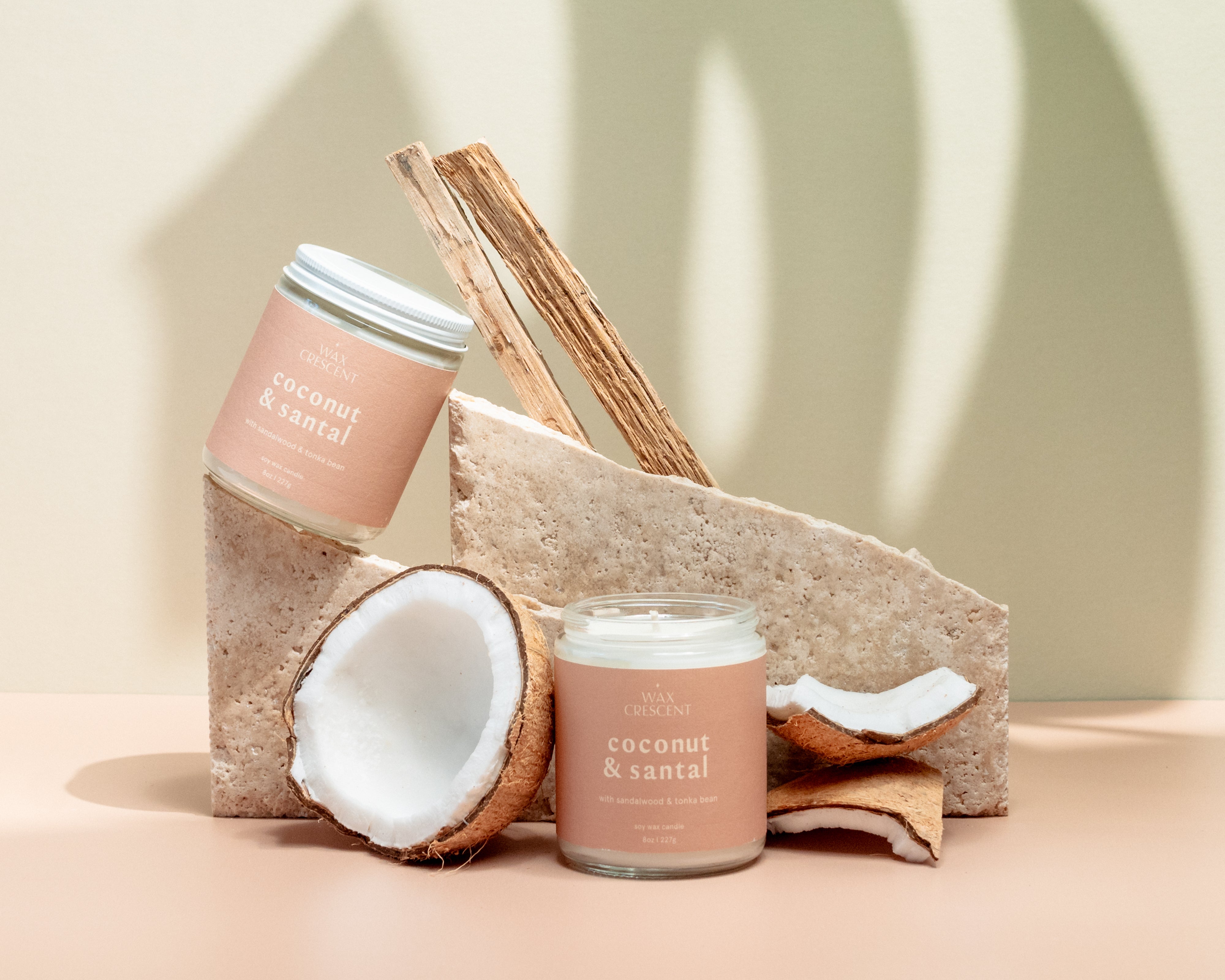 Wax Crescent Coconut & Santal candle styled with natural coconut shells, wood, and textured stone, set against a warm neutral backdrop for a tropical vibe.