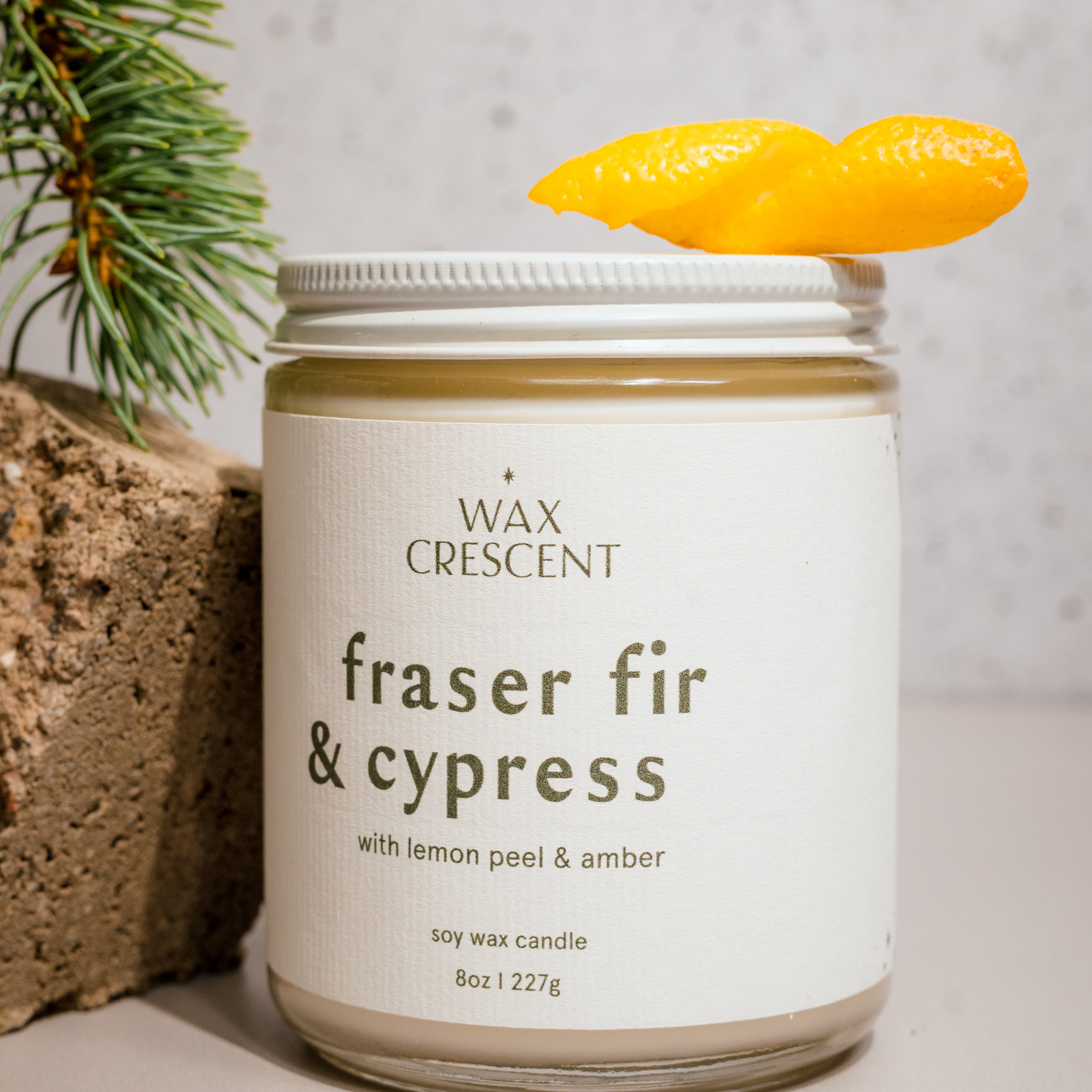 Fraser Fir & Cypress soy candle by Wax Crescent, surrounded by lemon peel and evergreen, evoking fresh, wintry forest aromas