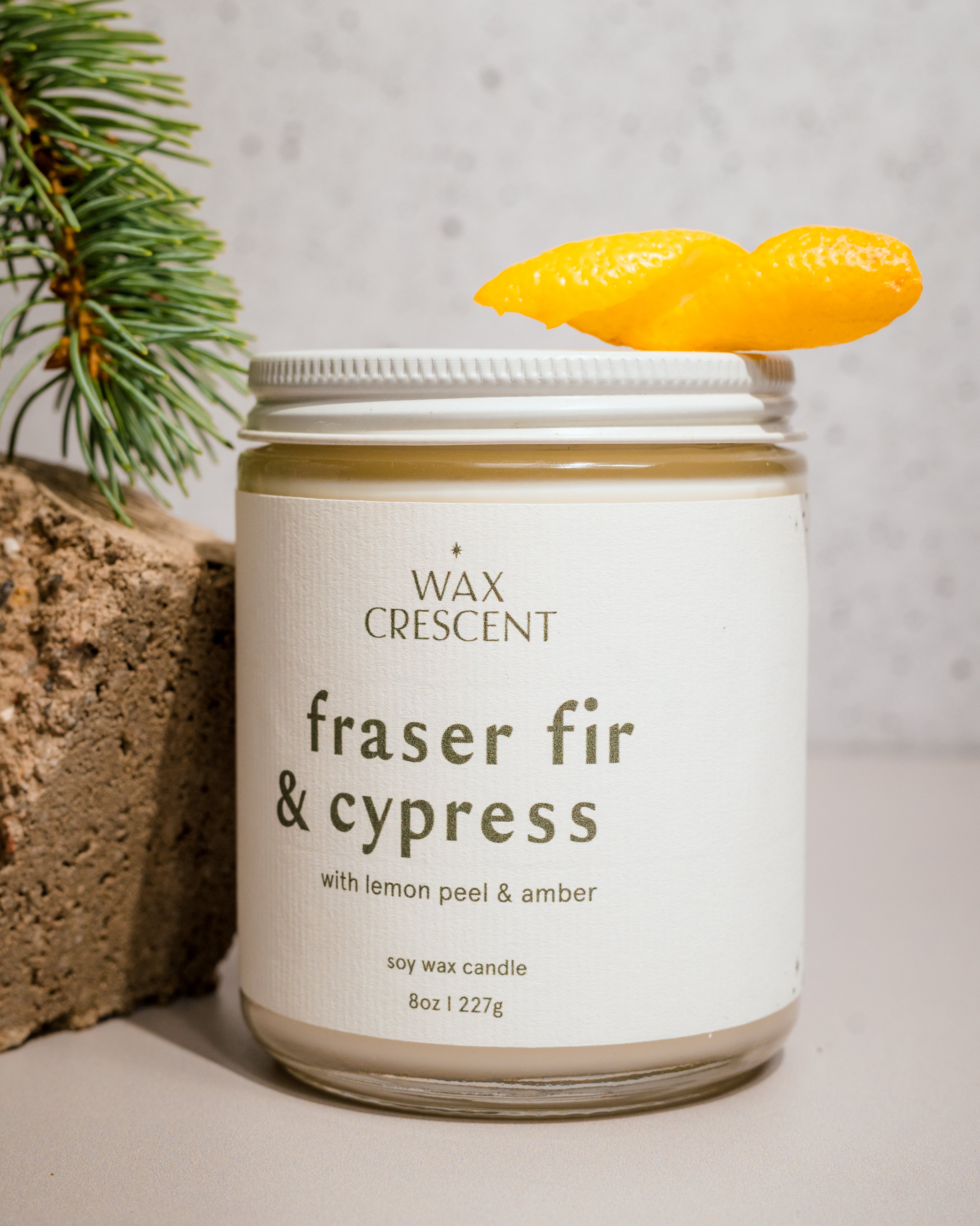 Fraser Fir & Cypress soy candle by Wax Crescent, surrounded by lemon peel and evergreen, evoking fresh, wintry forest aromas