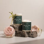 Wax Crescent's Glacier Rose & Ivy candles, featuring a green label with white text, elegantly displayed with a fresh rose and sage on dark stone blocks