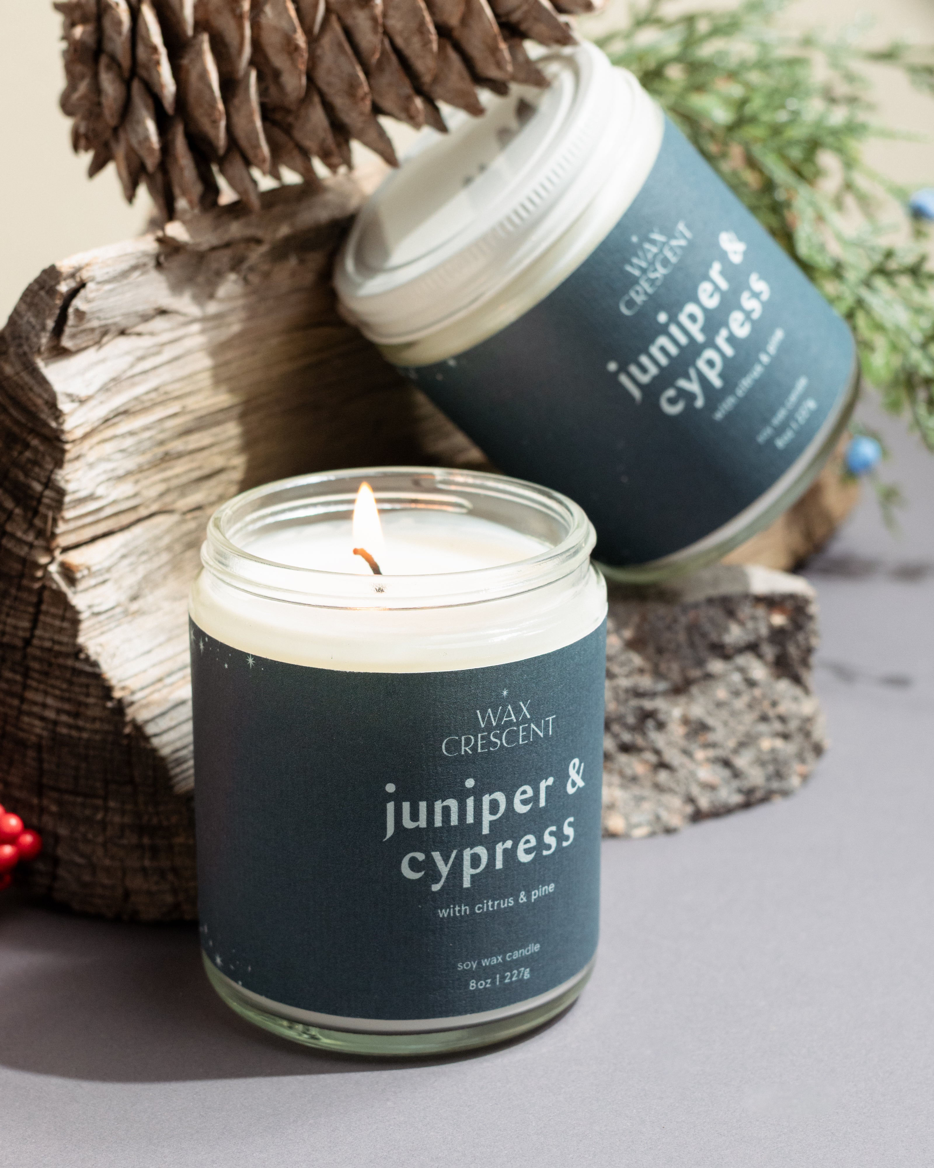 Pair of Juniper & Cypress candles with natural decorative elements on a neutral background — small-batch soy candles from Wax Crescent that bring fresh evergreen calm to any space