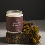 Side view of Leather & Suede candle, featuring masculine scent notes of leather, pine, and smoky embers, styled with natural moss