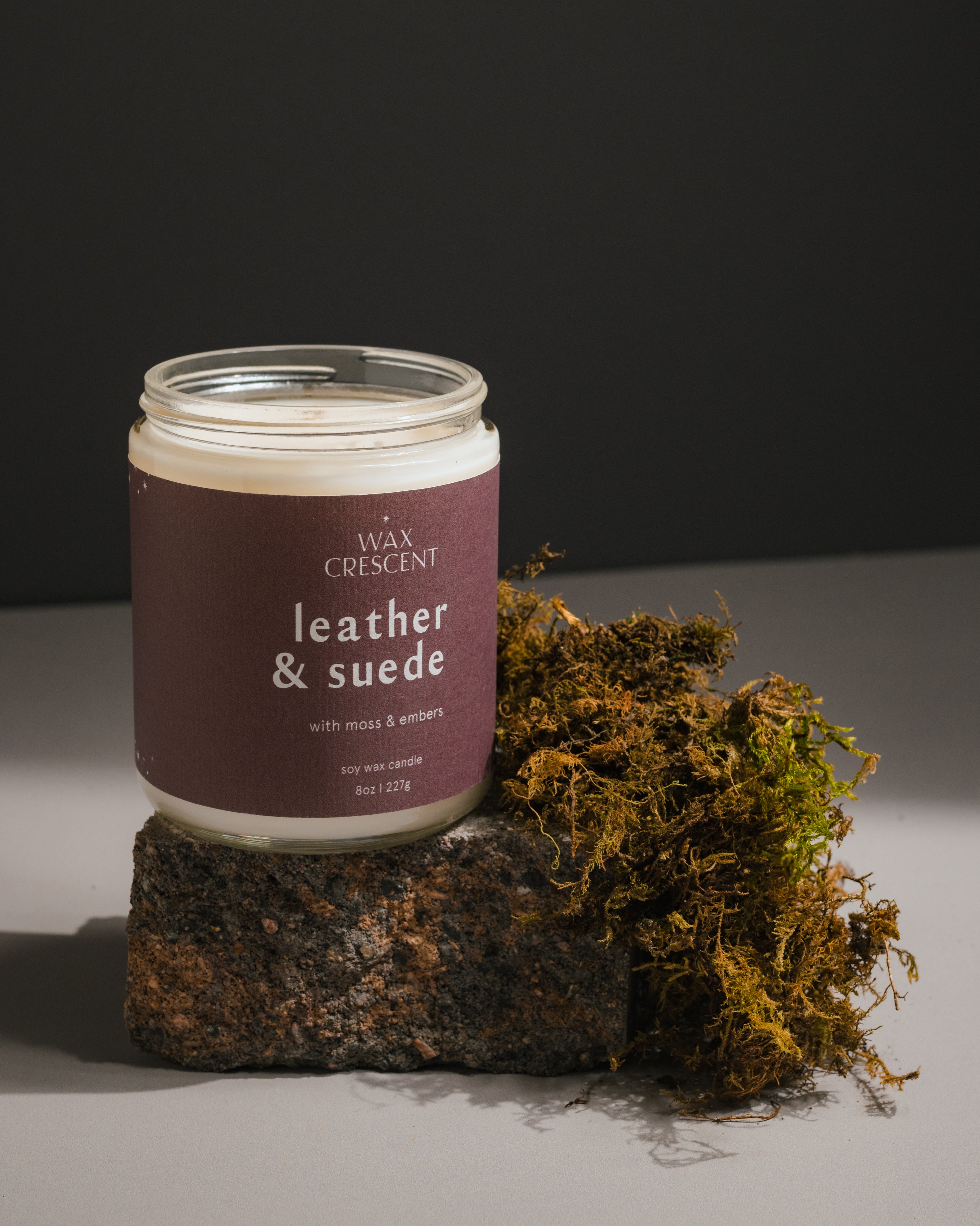 Side view of Leather & Suede candle, featuring masculine scent notes of leather, pine, and smoky embers, styled with natural moss