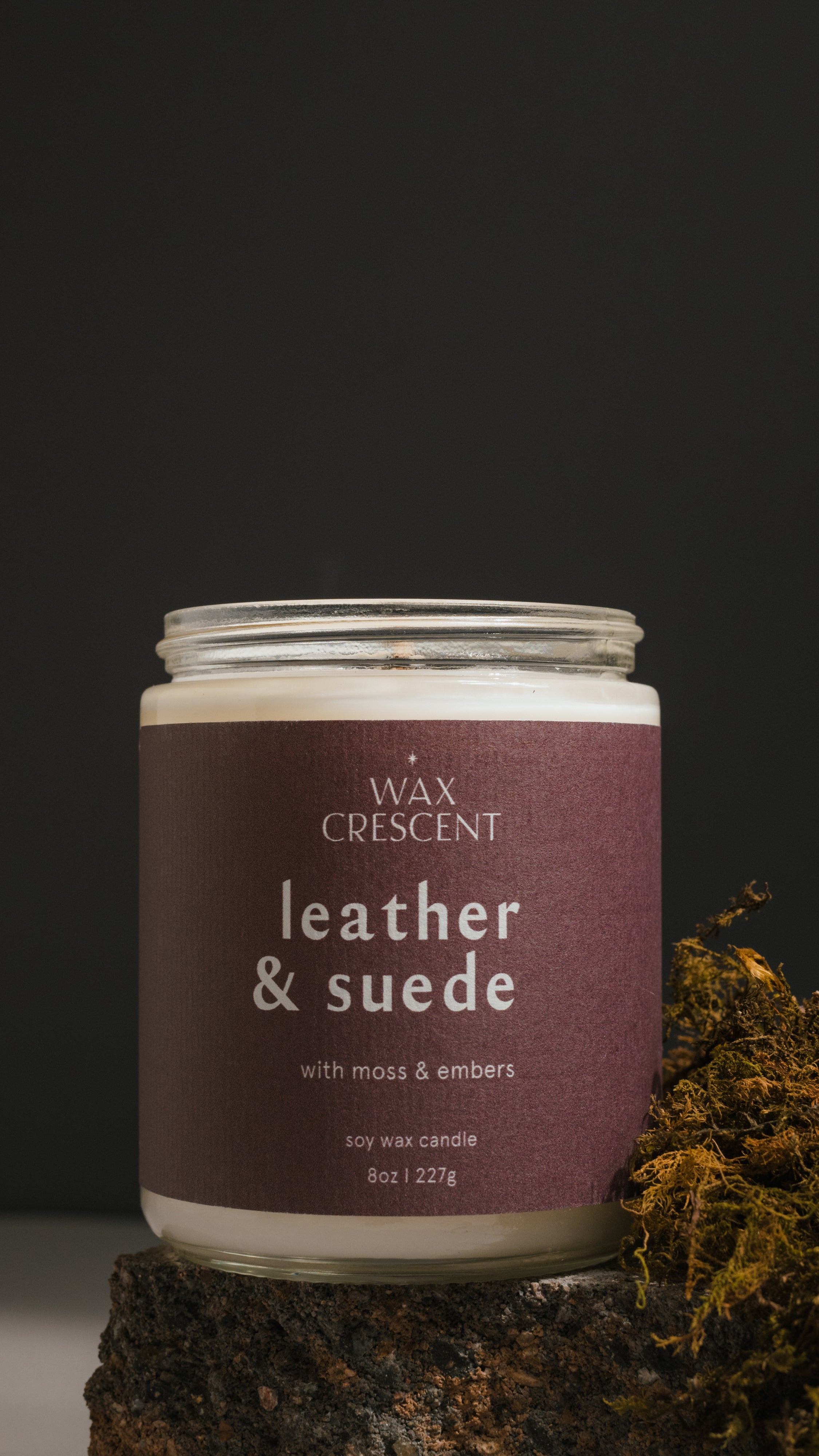 Close-up of Leather & Suede soy candle with rich notes of leather, clove, and cedar, styled with moss for a rugged look