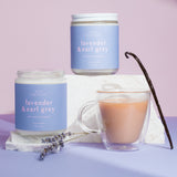 Two lavender-scented candles and a cup of tea on a purple surface with a light purple background.