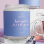 Two lavender and earl grey candles with a lavender flower on a purple background