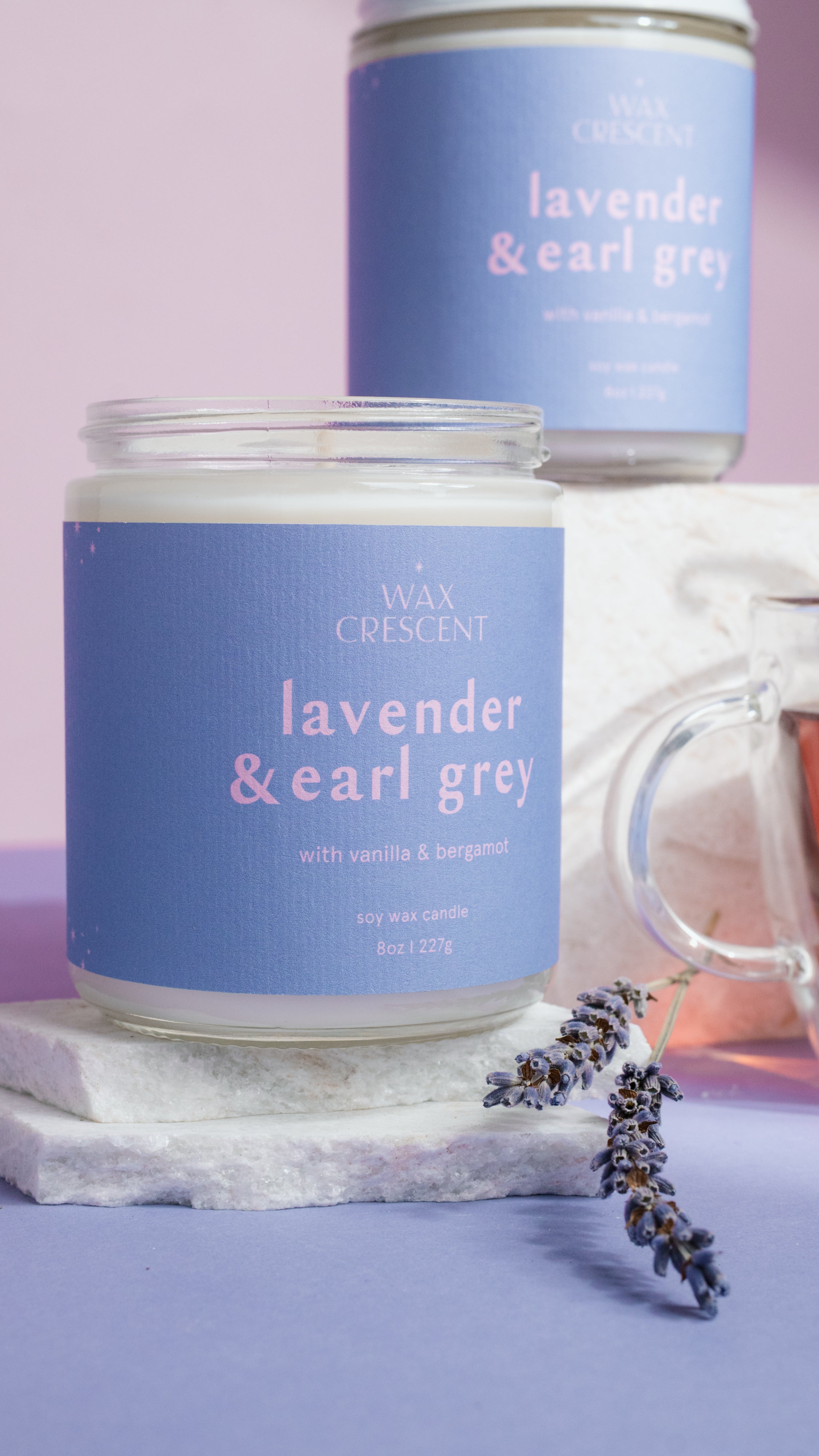 Two lavender and earl grey candles with a lavender flower on a purple background