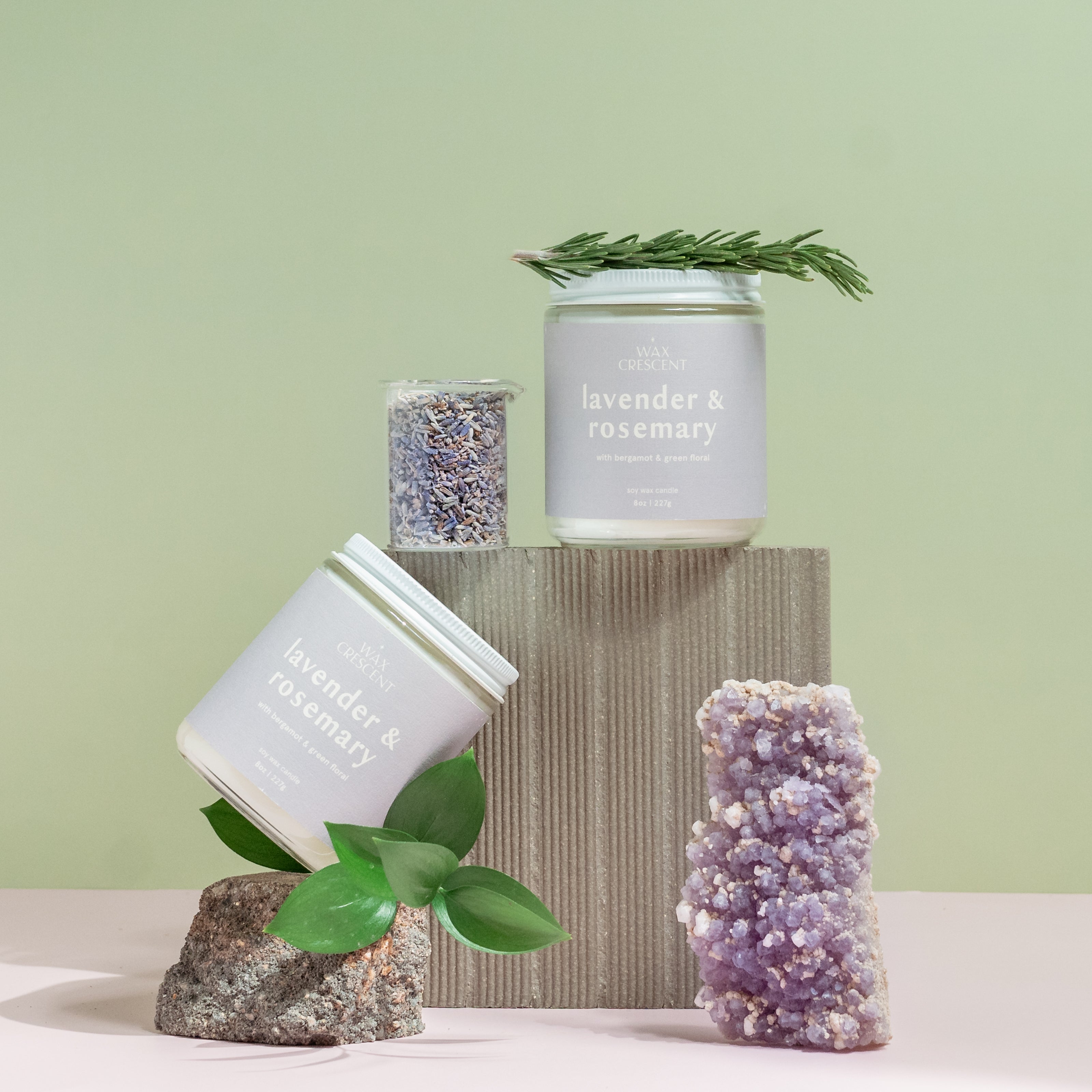 Wax Crescent Lavender & Rosemary candle styled with natural elements like lavender buds, rosemary sprigs, and amethyst crystal, set against a calming pastel backdrop