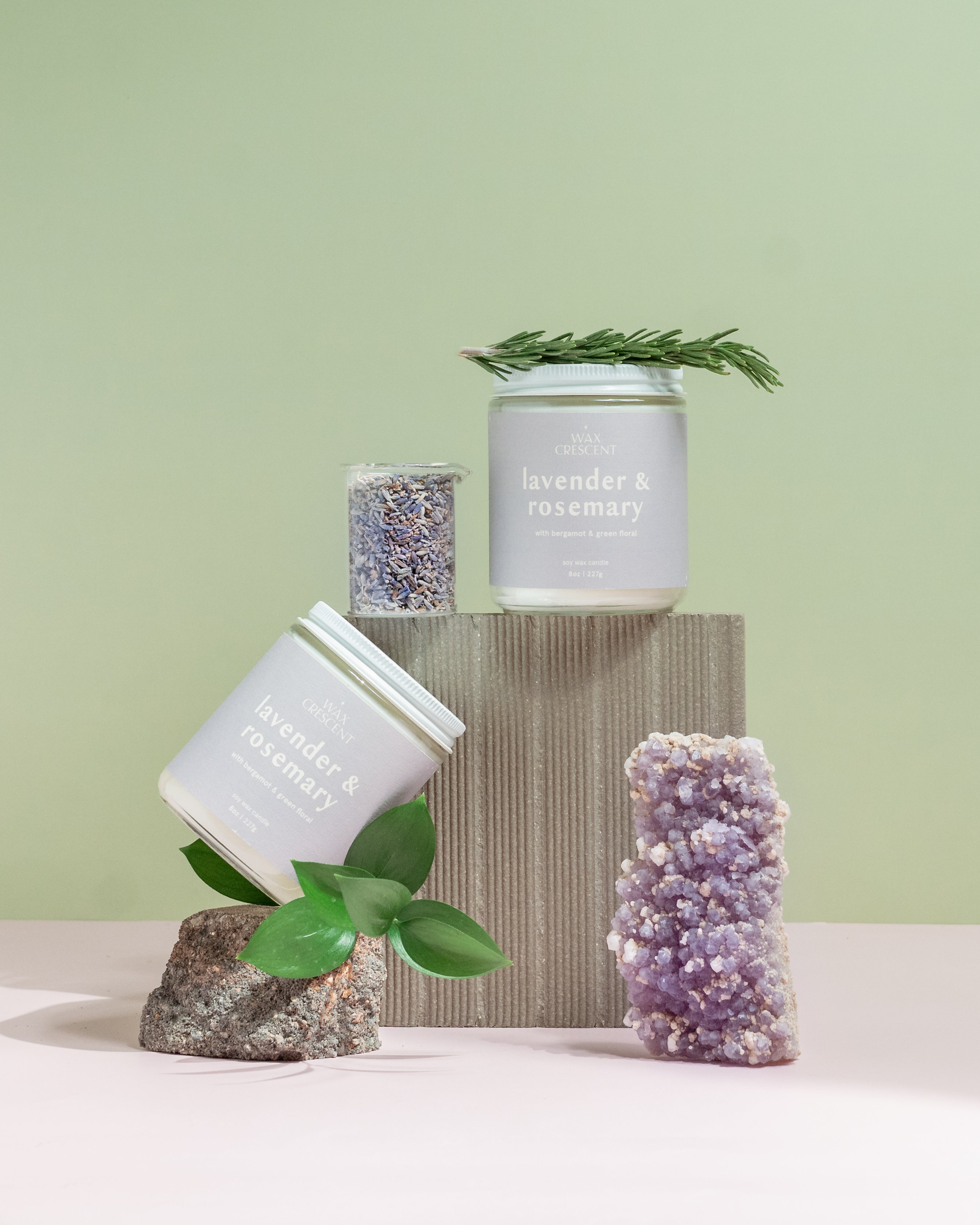 Wax Crescent Lavender & Rosemary candle styled with natural elements like lavender buds, rosemary sprigs, and amethyst crystal, set against a calming pastel backdrop