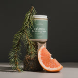 Oakmoss & Evergreen soy wax candle by Wax Crescent, hand-poured in Longmont, Colorado. Candle displayed with fresh evergreen sprigs and a grapefruit slice for a natural, clean-burning aromatherapy experience.