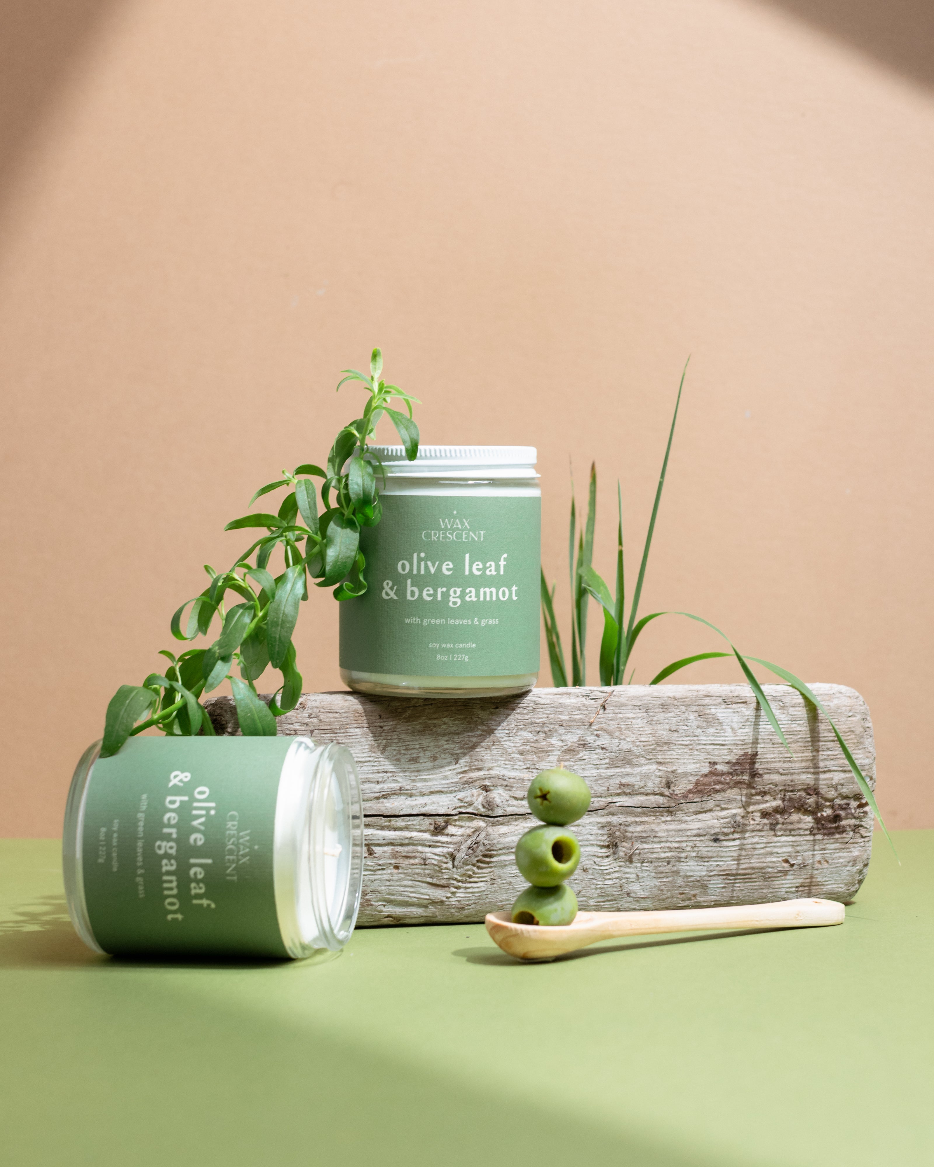 Two Olive Leaf & Bergamot soy candles with olive branches and fresh olives on a beige background — luxury hand-poured candles by Wax Crescent inspired by Mediterranean calm and golden light.