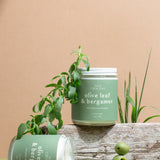 Two Olive Leaf & Bergamot candles on a beige background with olive branches and fresh olives — luxury soy candles hand-poured by Wax Crescent, featuring a clean, uplifting citrus and herbal scent inspired by Mediterranean elegance
