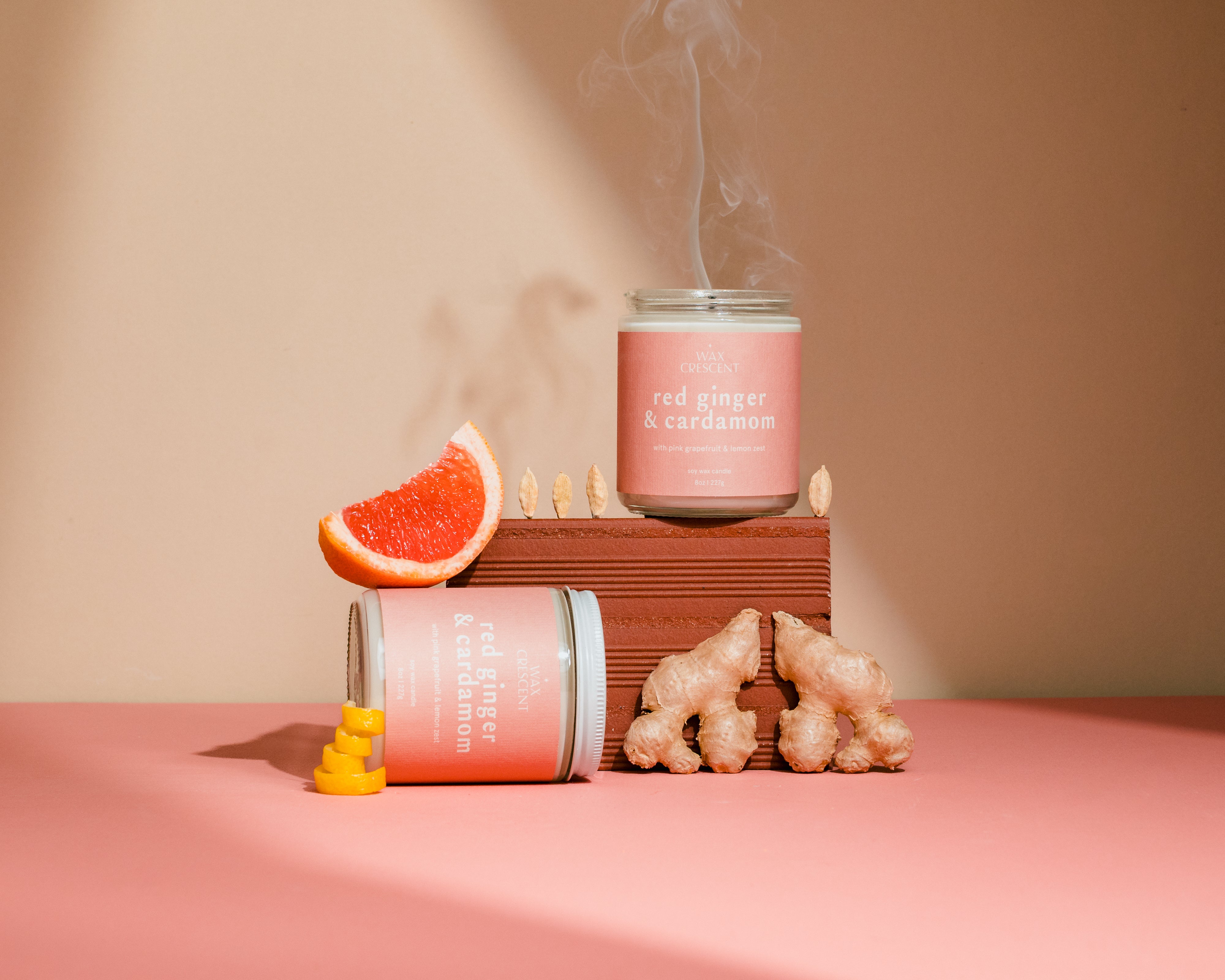 Pink candle labeled 'Red Ginger & Cardamom' with decorative elements on a pink surface.