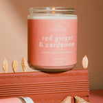 Wax Crescent candle labeled 'red ginger & cardamom' on a wooden block with ginger pieces.