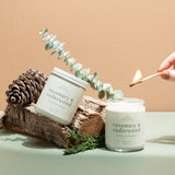 Hand-poured Rosemary & Cedarwood candle by Wax Crescent, surrounded by eucalyptus, pinecones, and rustic wood, evoking a serene and natural vibe.