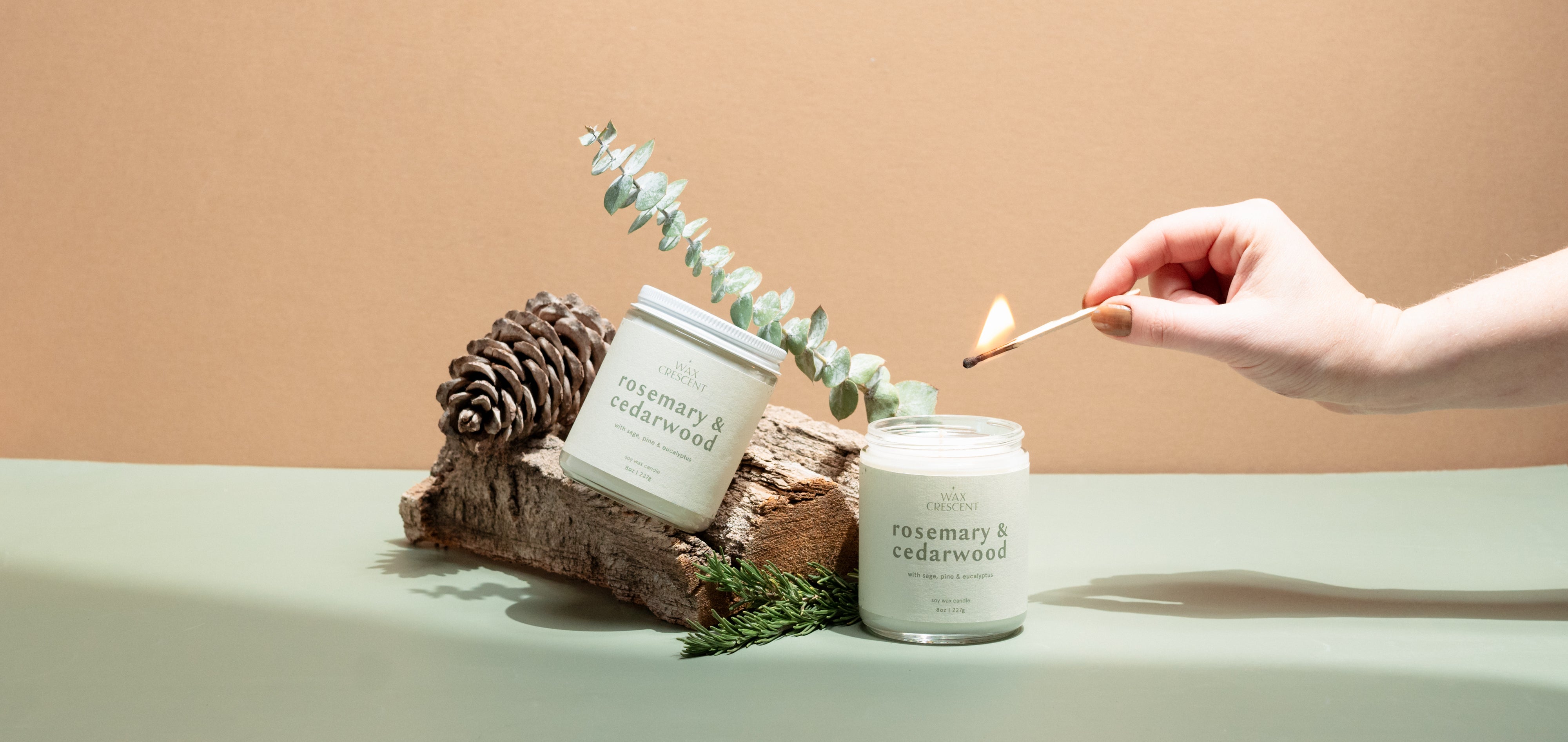 Hand-poured Rosemary & Cedarwood candle by Wax Crescent, surrounded by eucalyptus, pinecones, and rustic wood, evoking a serene and natural vibe.