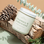 Close-up of Wax Crescent Rosemary & Cedarwood candle, styled with eucalyptus and rustic wood, showcasing its fresh, botanical scent and eco-friendly design