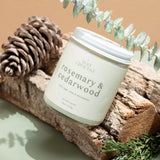 Close-up of Wax Crescent Rosemary & Cedarwood candle, styled with eucalyptus and rustic wood, showcasing its fresh, botanical scent and eco-friendly design