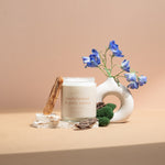 Wax Crescent Sandalwood & Palo Santo luxury soy candle surrounded by natural decor, including palo santo wood, moss, bark, and blue delphinium flowers, styled against a minimalist beige background. Perfect for creating a calming and meditative ambiance