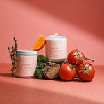 Hand-poured Tomato & Vetiver soy candle with tomatoes and orange accents on a pink background, evoking nostalgic garden-inspired scent notes.