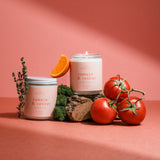 Hand-poured Tomato & Vetiver soy candle with tomatoes and orange accents on a pink background, evoking nostalgic garden-inspired scent notes.