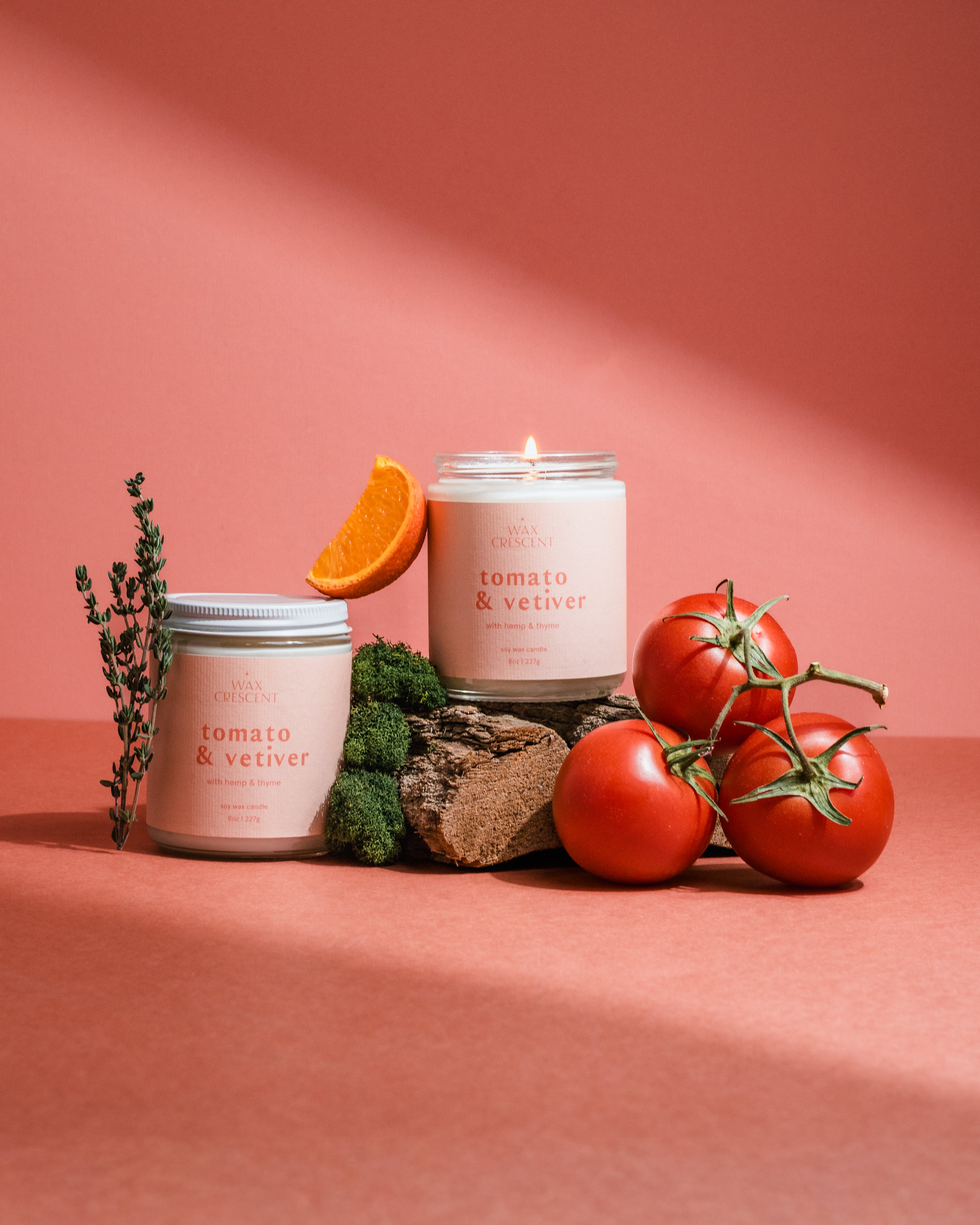 Hand-poured Tomato & Vetiver soy candle with tomatoes and orange accents on a pink background, evoking nostalgic garden-inspired scent notes.