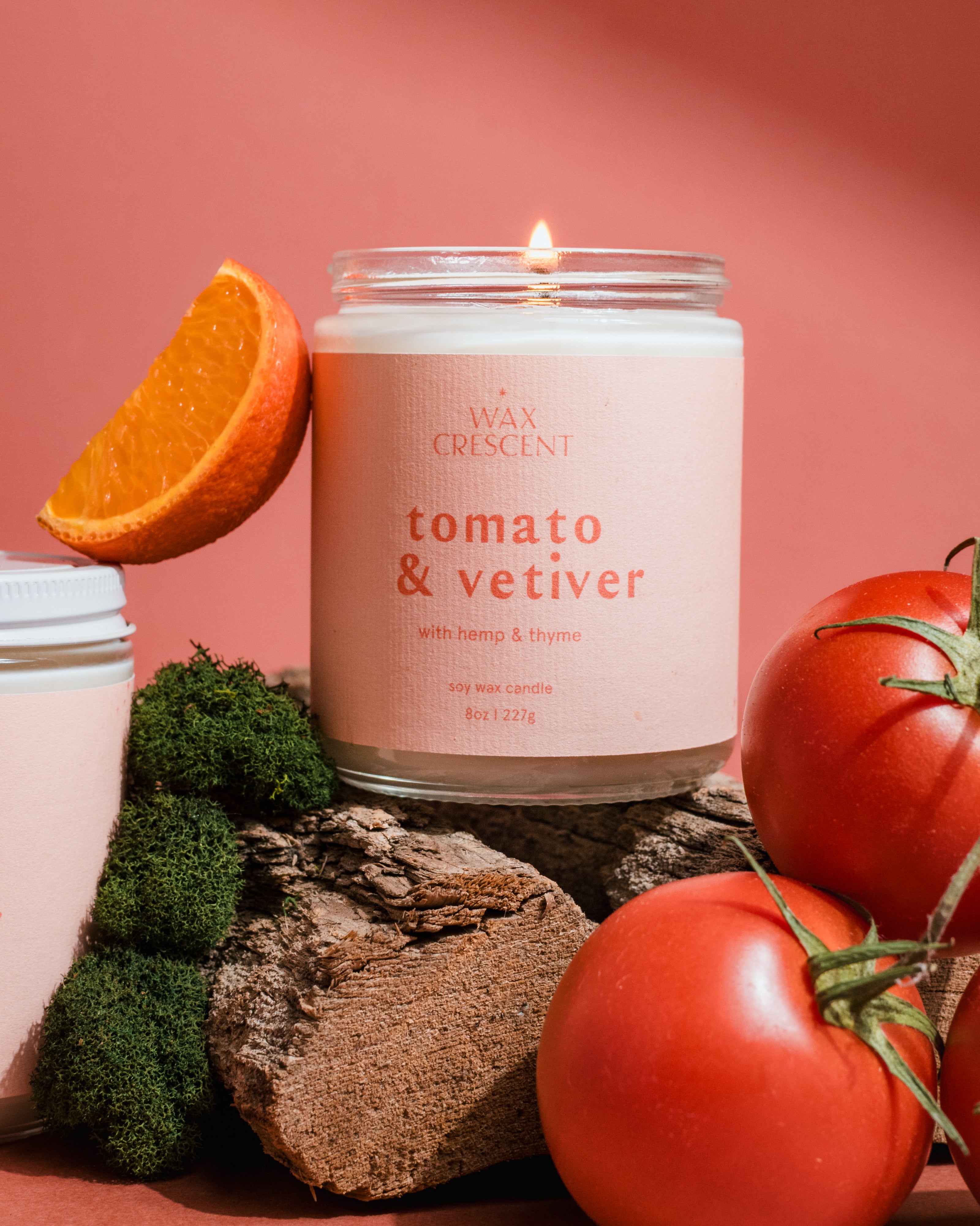 Modern luxury Tomato & Vetiver candle featuring fresh tomato vine inspiration with citrus and produce styling on a soft pink background.