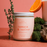 Clean-burning Tomato & Vetiver candle by Wax Crescent styled with fresh tomatoes and orange on a pink background for elevated summer home fragrance.