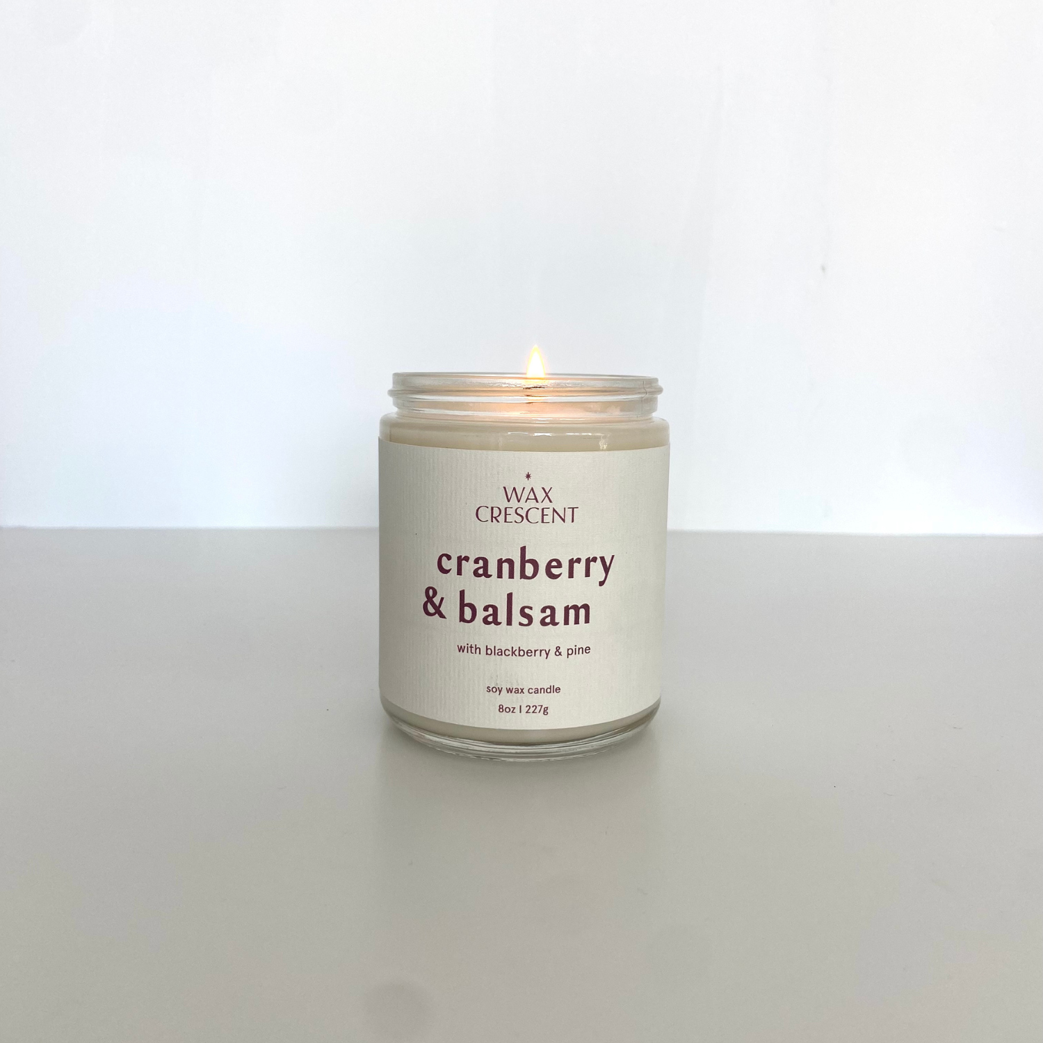 Cranberry & Balsam candle burning on a white background, showcasing a clean, elegant design and natural fragrance for home décor