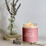 black fig and bergamot soy wax candle made with  all natural and eco-friendly soy wax burning with a bundle of lavender in the background 