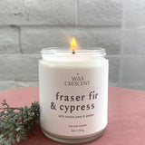 Fraser Fir & Cypress candle burning, set against festive greenery, perfect for adding a cozy and refreshing holiday aroma to any space.