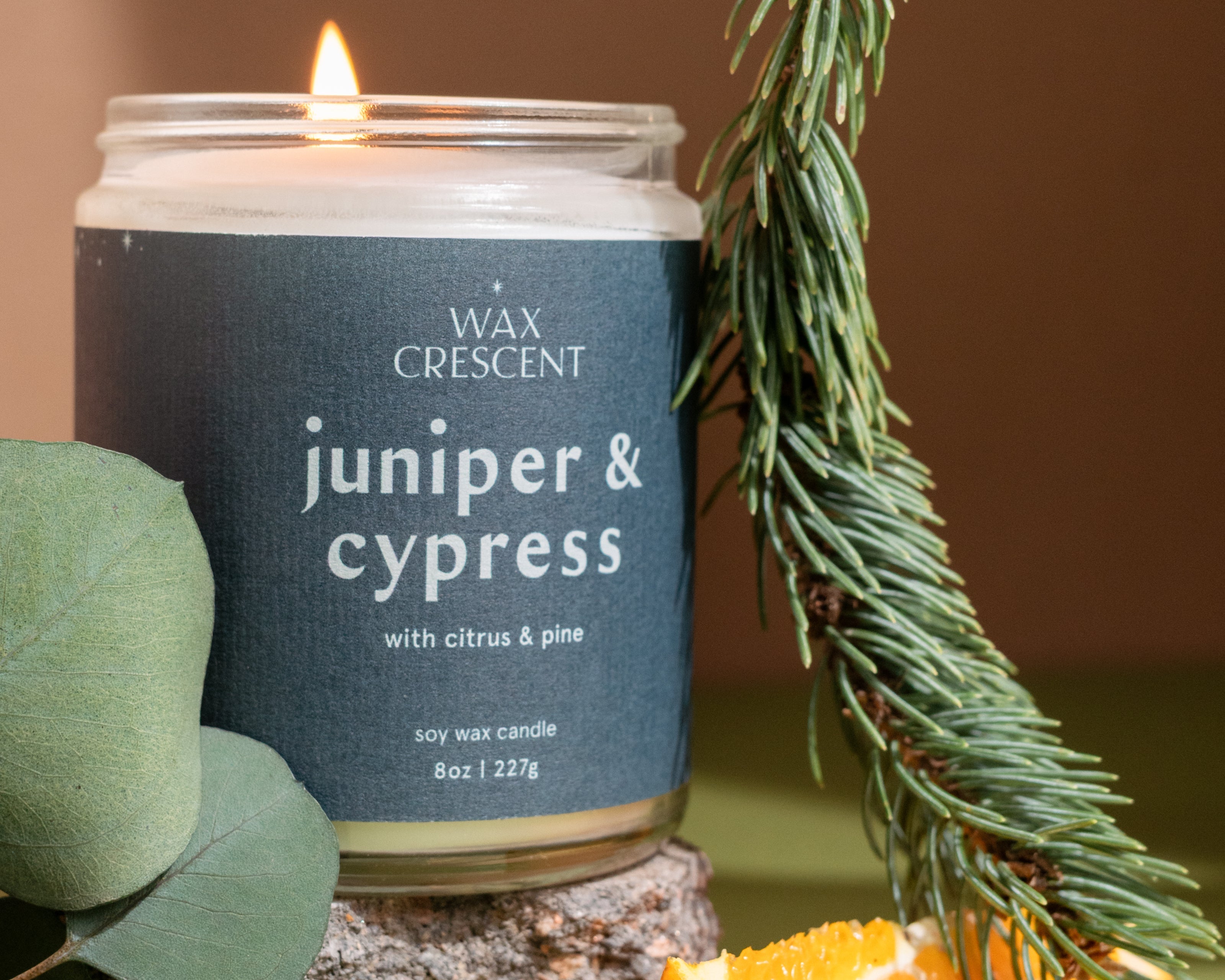 Two Juniper & Cypress soy candles surrounded by pine and juniper accents — clean, woodsy winter fragrance handcrafted by Wax Crescent for cozy seasonal ambiance.
