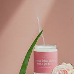 Wax Crescent Cactus Blossom & Rose Petals candle styled with aloe vera, soft pink rose, sand, and natural stones, set against a warm peach-toned background. the smoke from the candle is rising 