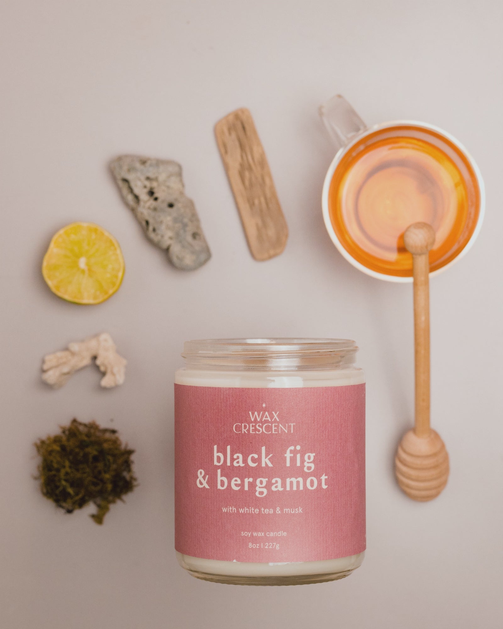 Stop-motion video of Black Fig & Bergamot candle with mauve label, featuring honey, lemon, ginger, and tea leaves moving around the candle.