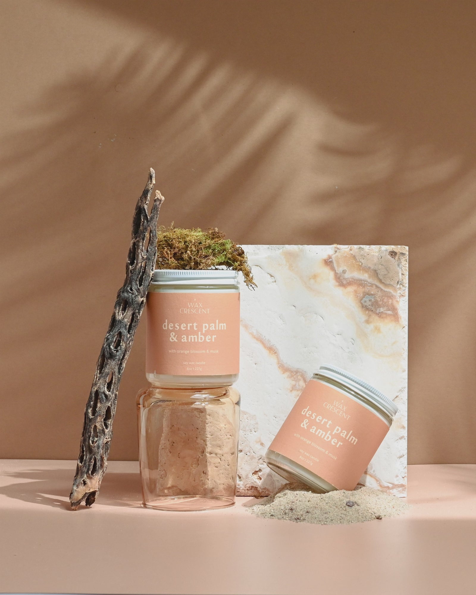 Desert Palm & Amber soy candle from Wax Crescent, surrounded by moss and natural elements, evoking a warm and serene desert-inspired ambiance.